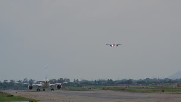 1機の飛行機は滑走路で離陸する準備をし もう1機は上陸のための降下段階にあり 空港活動と危険な空の背景に対して — ストック動画