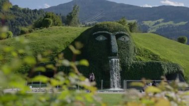 WATTENS, AUSTRIA - 13 Temmuz 2023: Avusturya 'daki Swarovski Müzesi' ndeki yeşil bir tepenin üzerine büyük bir heykel yüzünden su dökülüyor