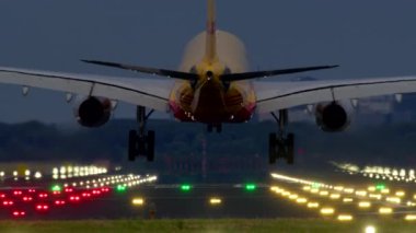 SCHIPHOL, NETHERLANDS - 25 AĞUSTOS, 2024: DHL uçağı alacakaranlıkta pist ışıkları ve arka planda uzak şehir binalarıyla bir piste yaklaşıyor