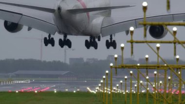Hava alanındaki bulutlu gökyüzünün altında ıslak bir piste iniş yapan büyük bir jetin yavaş çekim görüntüleri.