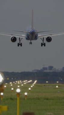 İniş için havaalanına doğru inen büyük bir uçağın yol gösterici ışıklarıyla podyuma yaklaştığının dikey videosu.