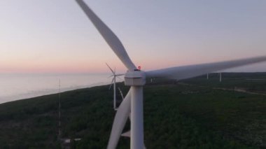 Renkli bir günbatımı gökyüzüne karşı dönen rüzgar türbininin yakın görüntüsü yenilenebilir enerji teknolojisini vurguluyor.