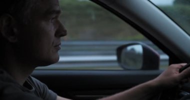 Erkek sürücü, akşam trafiğinin ve seyahatin dinamiklerini gözler önüne sererek, gün batımında otoyolda diğer araçların yanından geçiyor.