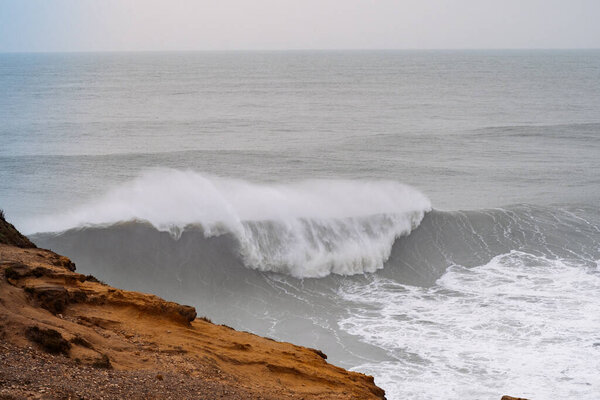 Мощная океанская волна ломается у скалистого побережья в португальском городе Назаре