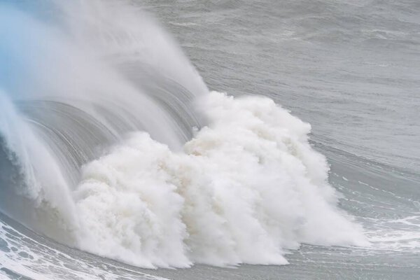 Огромные океанские волны, ползущие с пеной и брызгами на Назаре в Португалии