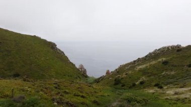 Portekiz Cabo da Roca 'da sisli bir okyanus manzarasına yol açan tepeler tarafından çevrelenmiş yemyeşil bir vadi.