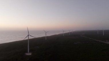 Rüzgar türbinleri kıyı şeridinde temiz enerji üretir. Güneş batar ve karaya sıcak bir ışıltı saçar.