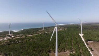 Güneşli bir günde, arka planda okyanus varken rüzgar türbini döner ve yenilenebilir enerji üretir.