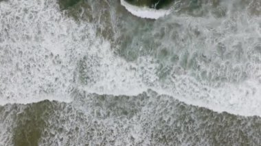 Beyaz deniz dalgaları acımasız bir şekilde kumlu bir plaja çarpar ve büyüleyici bir güç ve güzellik gösterisi yaratır.
