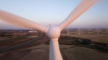 Temiz enerji üreten rüzgar türbini kırsal bir arazide dönüyor, bir otoyol ve doğanın güzelliğini gösteriyor.