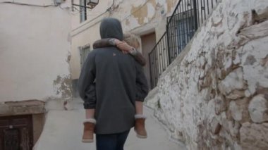 Bir abi, uyuyan küçük kız kardeşini dar bir sokakta taşır.