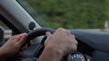 Direksiyona odaklanmış eller ön paneli ve ön camdan geçen yolu net bir şekilde görüyor.