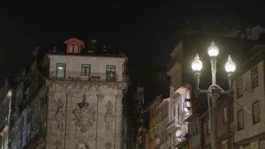 Porto, Portekiz 'de geceleri aydınlatılan, karmaşık oymaları ve kırmızı bir çatı penceresi olan tarihi bir taş bina. Geleneksel mimari ve ışıldayan sokak lambalarıyla çevrili.