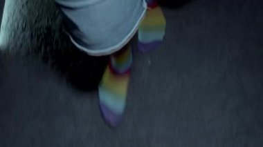 Karanlık yüzeyde canlı gökkuşağı çorapları içinde yürüyen kendinden emin bir erkek cesur moda seçimiyle kişisel stili ve gururunu sergiliyor.