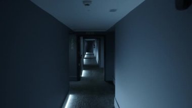 Loş ışıklandırılmış otel koridoru, içinde oda numaraları olan bir dizi kapı gösteriyor. Gizem ve entrika dolu bir atmosfer yaratıyor.