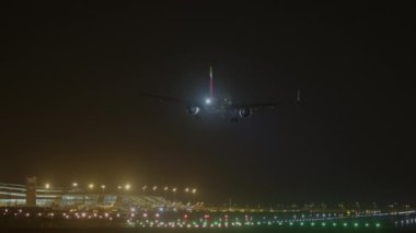 Uçak gece aydınlık bir havaalanı pistine iniyor, havacılık ve gece operasyonları gösteriliyor.