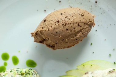 Close-up of gourmet liver pate sprinkled with black pepper on a plate with green apple slices and herbed garnish clipart