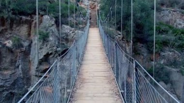 Tahta Tibet köprüsü kayalık vadiyi kaplıyor, geniş panoramik manzaraları gözler önüne seriyor ve dramatik manzara perspektifinden maceraperest vahşi doğa keşiflerini çağrıştırıyor.