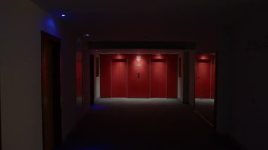 Kıpkırmızı asansör kapılarının olduğu loş bir otel koridoru gizemli gölgeler yaratıyor, gözle görülür belirsizlik ve gizemli atmosfer gerilimi yaratıyor.