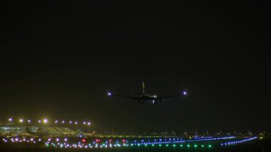Gece saatlerinde ışıl ışıl parlayan piste inen yolcu jeti, şehir manzarası ve ışıl ışıl şehir ışıkları havacılık yaklaşımı için dramatik bir zemin oluşturuyor.
