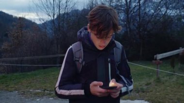 Genç bir gezgin, akıllı telefonuyla Pireneler parkında sırt çantasıyla dolaşırken, kış akşamları doğal manzaranın ortasında dijital bir anı yakalıyor.