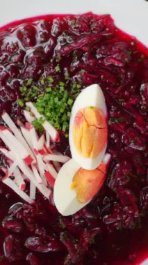 Dikey görüntüler geleneksel Ukrayna borş çorbası, haşlanmış yumurta, taze turp ve soğanla süslenmiş canlı pancar tabanlı bir yemek, çeşitli yakın çekim çekimlerinde sunuluyor.