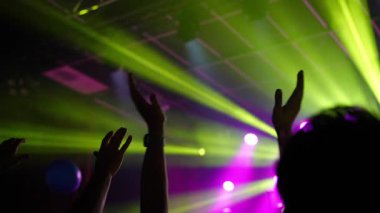 Coşkulu müzik hayranları, canlı performans sırasında canlı performansları aydınlatan renkli sahne ışıklarıyla enerjik bir kalabalık atmosferi yaratıyor.