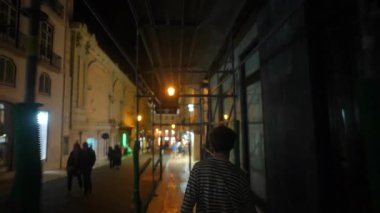 Gece şehir caddesinde iskelenin altından atlayan bir genç, ışıklar ve binalar eşliğinde arkadan filme alındı.