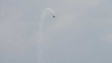 Küçük akrobatik uçak bulutlu gökyüzünde beyaz bir duman iziyle bir döngü gerçekleştirir.