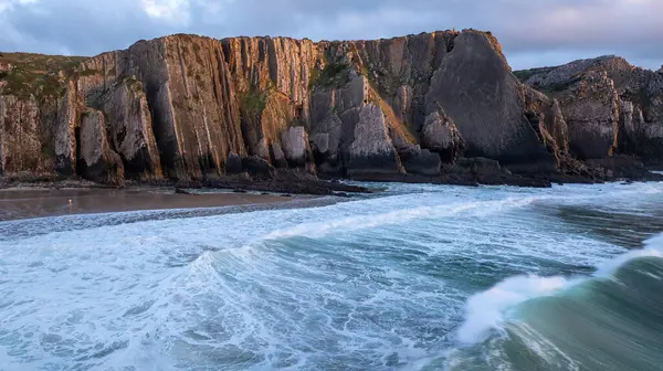 Okyanus dalgaları günbatımında Praia da Adraga sahiline çarpıyor. Arka planda ise Sintra, Portekiz 'de kayalıklar var.