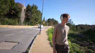 Gündüz kıyafetleri içinde gezen, kulaklık takan, yeşillik ve sakin bir atmosferle çevrili genç, sakin bir doğa deneyimi sergiliyor.