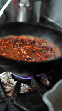 Yemek pişirme sürecinde haşlama sosu ve canlı sebzelerle dolu bir tava, gaz sobası üzerinde lezzet ve dokuların kademeli olarak harmanlanarak zengin bir mutfak deneyimi yaratıyor.