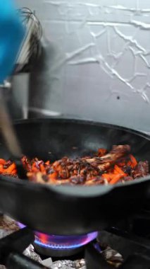 Yemek pişirme süreci tavada sotelenen sığır eti ve havuçları gösteriyor, canlı bir alev üzerinde karamelize ederken canlı renkleri ve dokuları vurguluyor, iştah açıcı bir mutfak sahnesi yaratıyor.