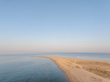 Güneş doğarken Yunanistan 'ın Khalkidhiki kentindeki güzel bir kumlu tükürüğün yanında demirlemiş bir yelkenlinin nefes kesici hava manzarası huzurlu ve huzurlu bir manzara yaratıyor.