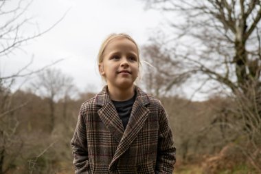 Palto giyen düşünceli bir çocuk, kış boyunca sakin bir ormanın ortasında duruyor. Doğadaki merak ve merakı somutlaştırıyor.