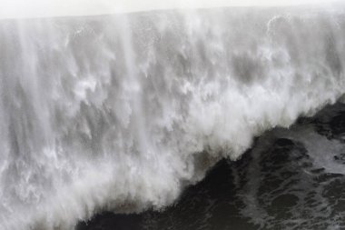 Çalkantılı okyanus dalgaları çarpıyor, beyaz köpükleri karanlık gökyüzüne püskürtüyor, fırtınalı havalarda güçlü deniz kuvvetlerini açığa çıkarıyor.