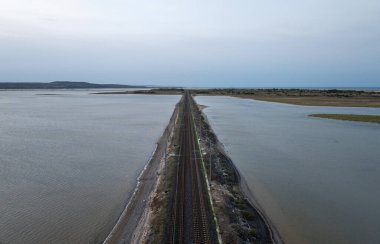 Fransa 'nın Occitanie kentindeki Leucate yakınlarındaki Etang de Leucate lagününden geçen bir demiryolu hattının havadan görünüşü bir yok oluş noktası yaratıyor.