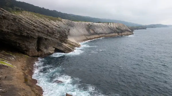 Cantabrian denizinin güçlü dalgaları bulutlu bir günde Llanes, Asturias, İspanya 'nın kayalık kayalıklarına çarpıyor.