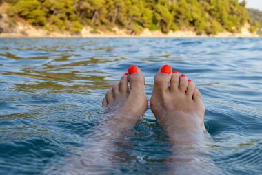 Kadınsı ayak parmakları güneşli sahil anında turkuaz kıyı sularına uzanan parlak turuncu renge boyanmış.