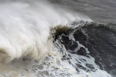 Güçlü deniz enerjisiyle yoğun fırtınalı deniz manzarası sırasında devasa okyanus dalgaları çarpar, dramatik beyaz köpük üretir.