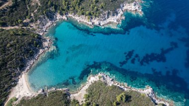 Yunanistan 'ın Toroni kentinde canlı yeşil bir sahil şeridiyle çevrili, kristal berrak turkuaz suyu bulunan tenha bir körfezin havadan görünüşü
