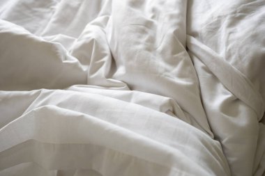 Uyandıktan sonra kırışıklıklarla dolu dağınık beyaz yatak çarşaflarını kapat, rahat ve rahat bir yatak odasını temsil ediyor.