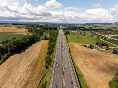 Avusturya 'nın aşağısındaki otobandaki arabaların hava manzarası yaz güneşi altında tarlaları ve ağaçları geçiyor. Orta Avrupa 'da düzgün bir asfalt otoyol. Yeşil alanlar ve mavi gökyüzünün yüksek açılı perspektifi