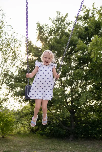 Mutlu çocuk bir parkta salıncakta sallanıyor, yaz tatillerinin tadını çıkarıyor ve açık hava maceralarını kucaklıyor.