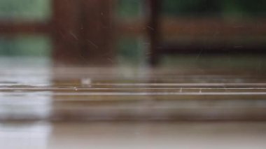 Yağan yağmur damlalarından akan sular yağmur sırasında ahşap terasa çarpar.