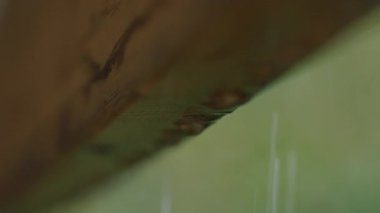 Yağmur suyunun yakın çekimi, ahşap çatı yapısının kenarından yavaşça damlıyor.