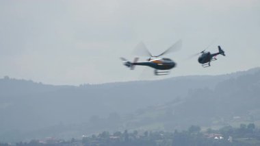 Gündüz vakti sisli bir dağ üzerinde uçan iki helikopter.