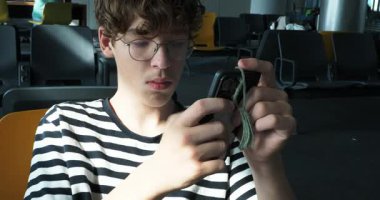 Havaalanındaki kalkış salonunda telefon kullanan çizgili tişörtlü bir genç.