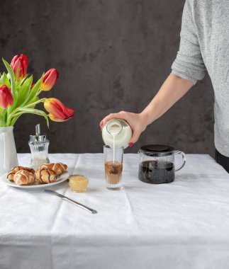 Womens hands pour milk into coffee. Breakfast is on the table.