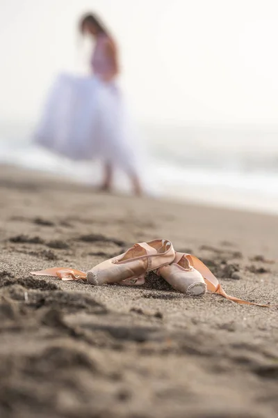 Pointe shoes on the sand , a ballerina in the background